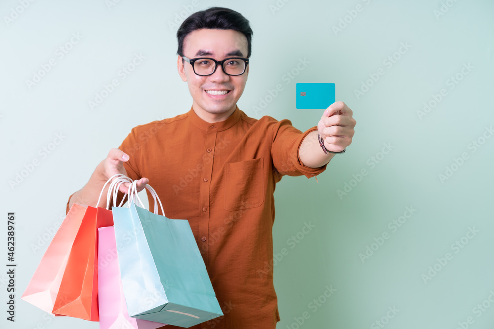 Young Asian man holding shopping bag on green background