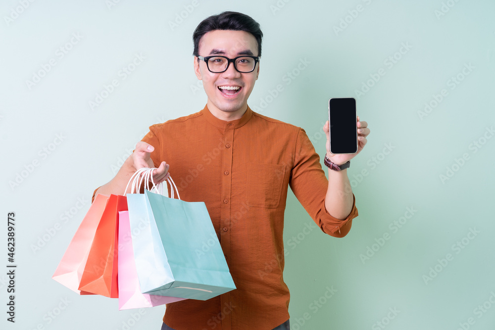 Young Asian man holding shopping bag on green background