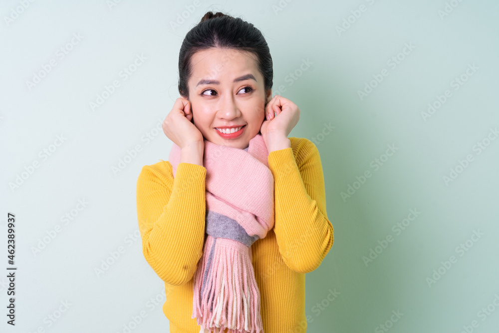 Beautiful young Asian woman wearing sweater on green background