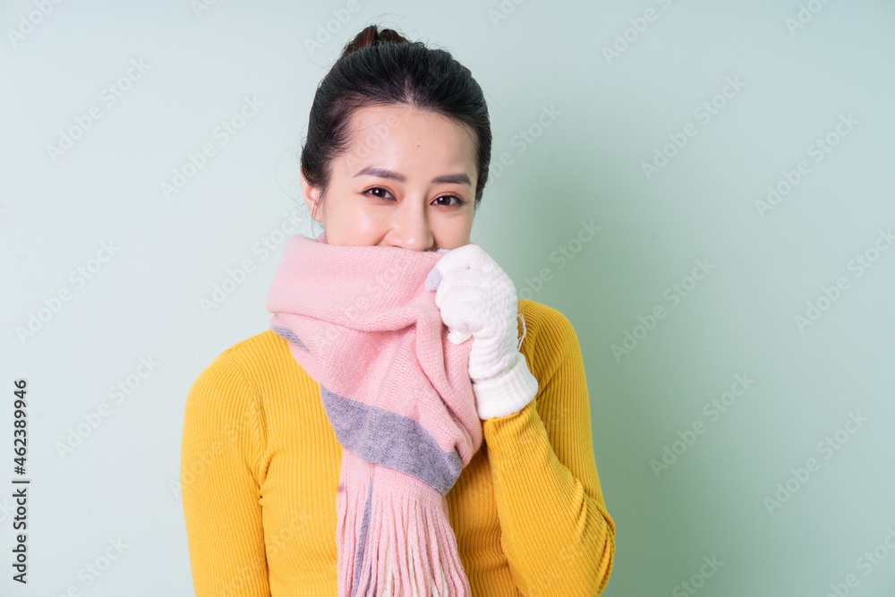 Beautiful young Asian woman wearing sweater on green background