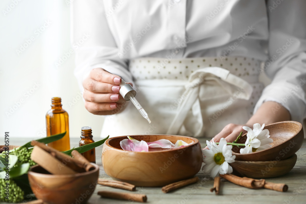 Woman adding essential oil to water in bowl on table