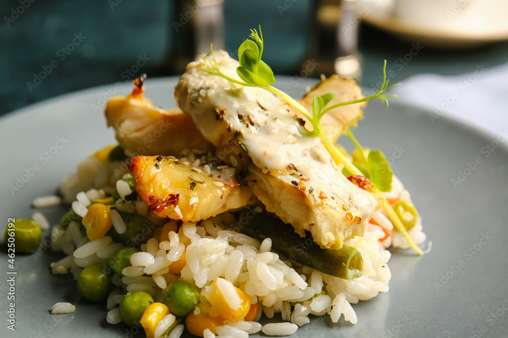 Plate with tasty baked cod fillet, rice and vegetables on table in restaurant, closeup