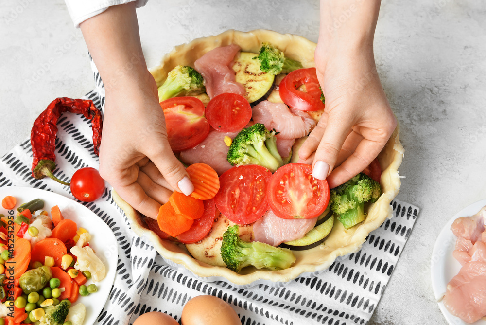 Woman preparing chicken pot pie with vegetables on light background