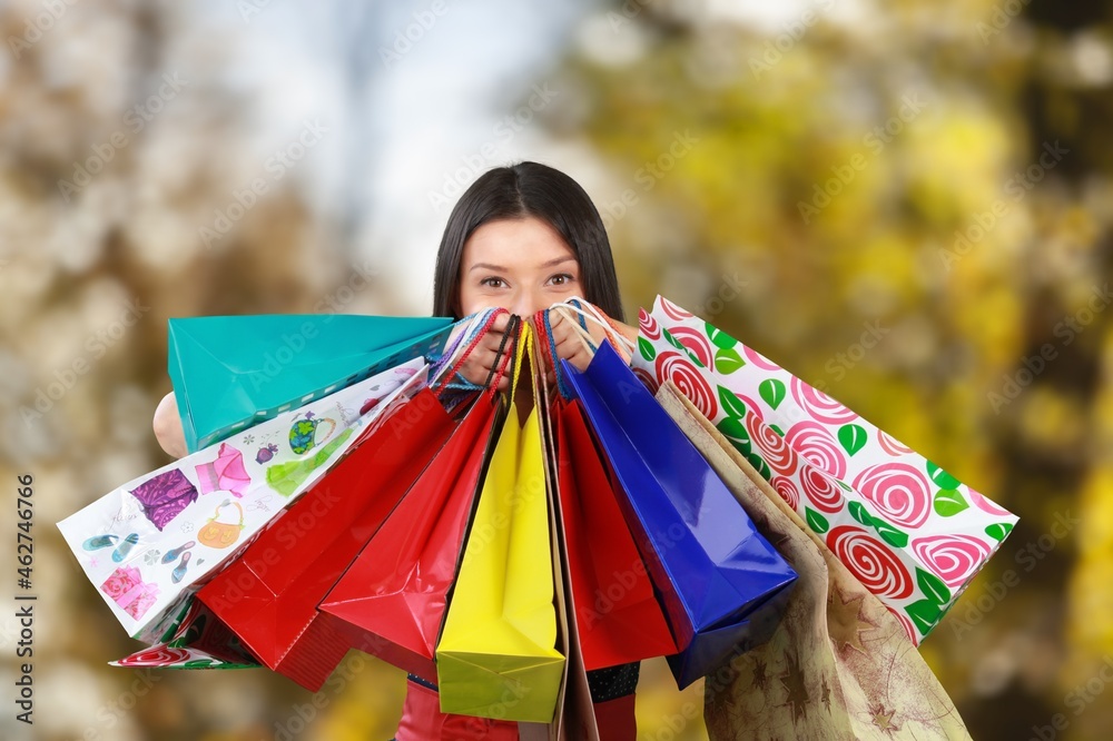 Happy elegant woman with shopping bags and autumn yellow background