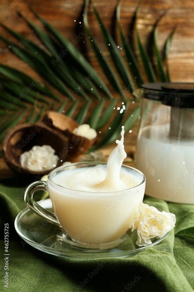 Cup of coconut milk with splash and flower on table