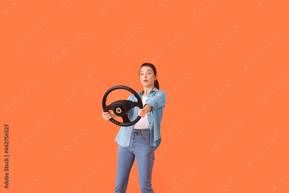 Shocked young woman with steering wheel on color background