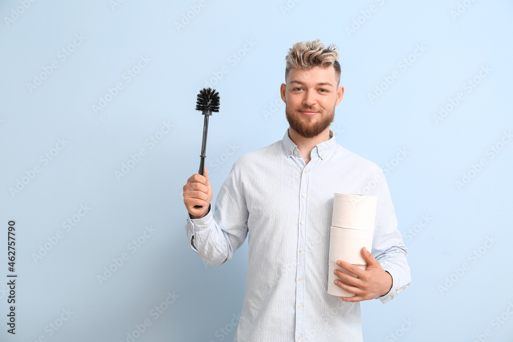 Young man with toilet brush and paper on color background