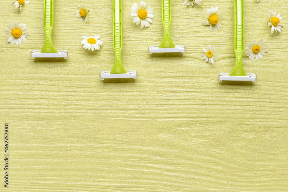 Safety razors and chamomile flowers on color wooden background, closeup