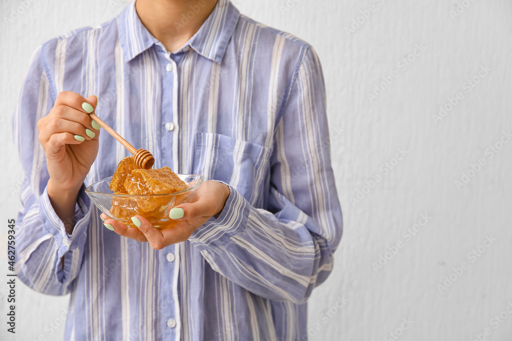 Woman holding bowl of honey combs with dipper on light background, closeup