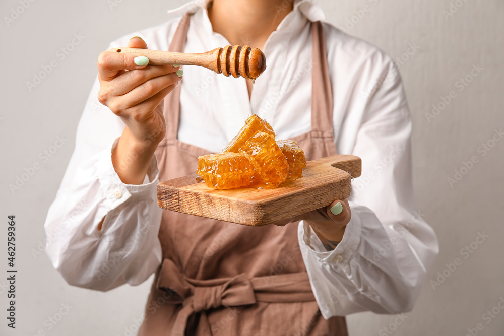 Woman pouring honey onto combs on light background, closeup