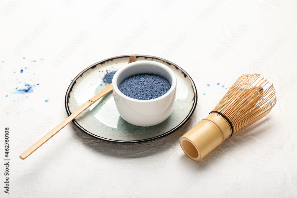 Bowl of powdered blue matcha tea, chashaku and chasen on light background