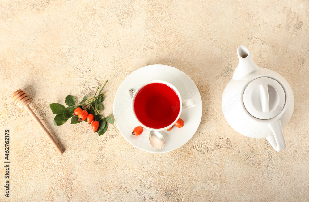 Cup of tasty rose hip tea, pot, berries and dipper on light background