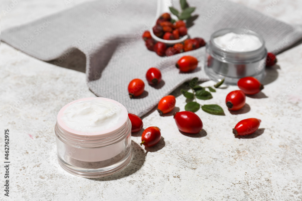 Jars of cosmetic products and rose hip berries on light background