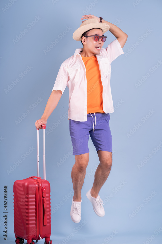 Young Asian man holding red suitcase on blue background