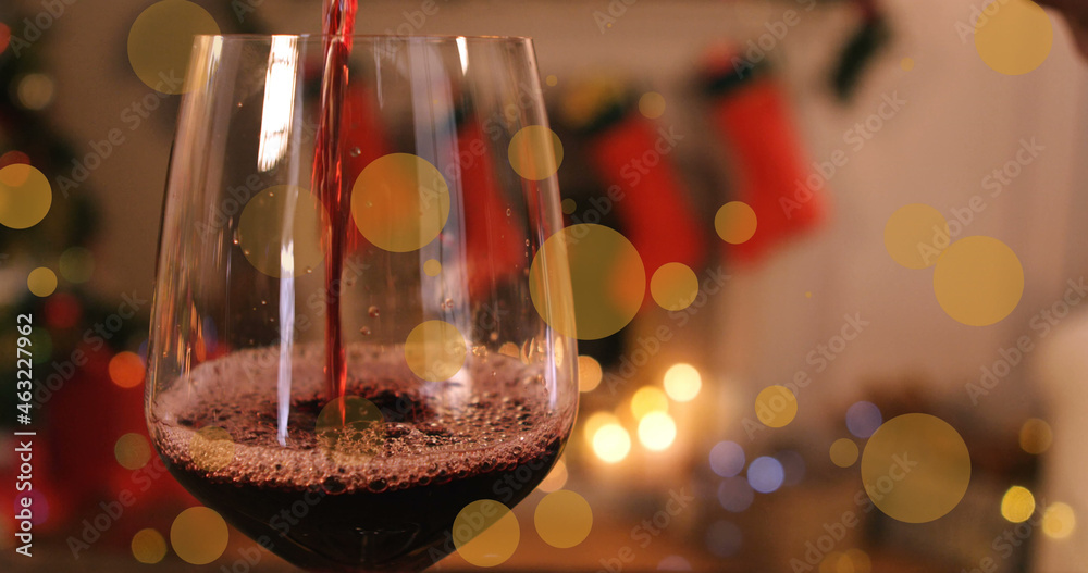 Image of glowing spots over glass of red wine and christmas decorations