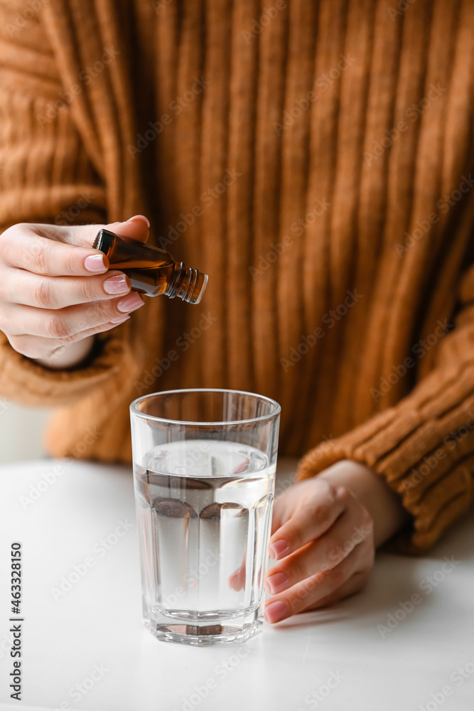 女人在桌子上的玻璃杯里往水中添加精油