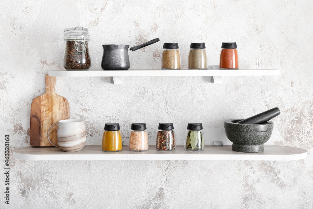 Jars with different spices, coffee beans and kitchen utensils on shelves