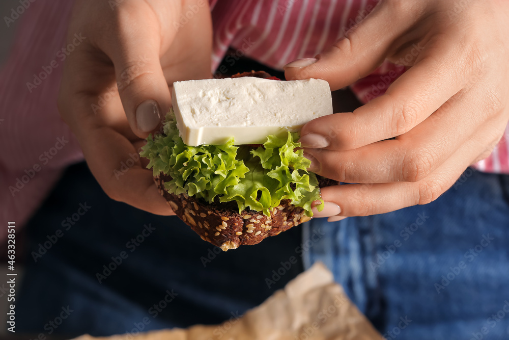 Woman making sandwich with feta cheese in kitchen