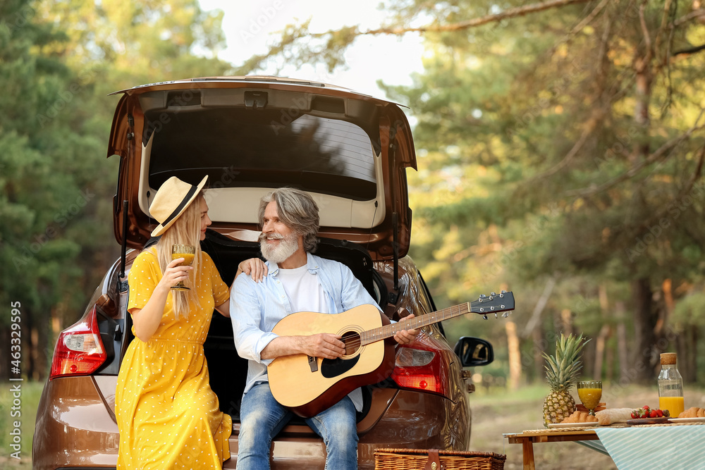 Mature man playing guitar for his wife near car in forest