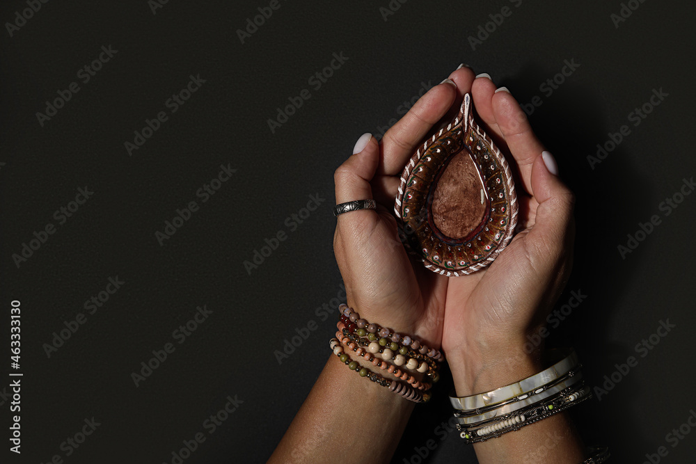 Female hands with diya lamp for Diwali on dark background