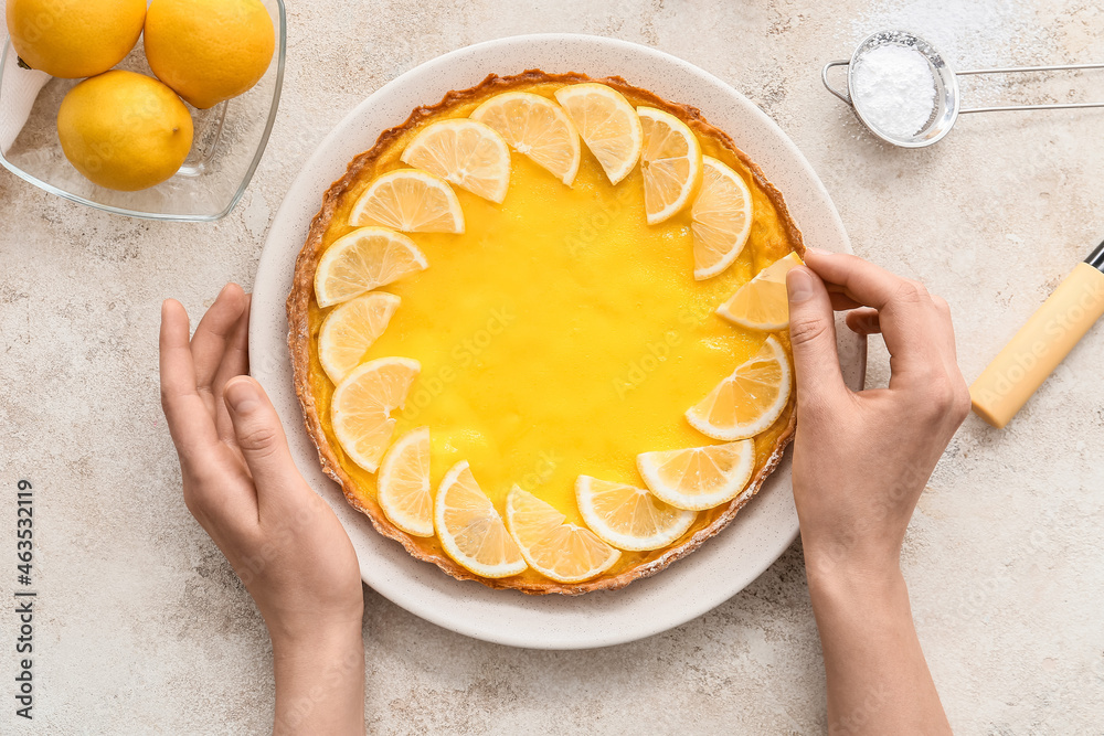 Woman decorating tasty lemon pie on light background