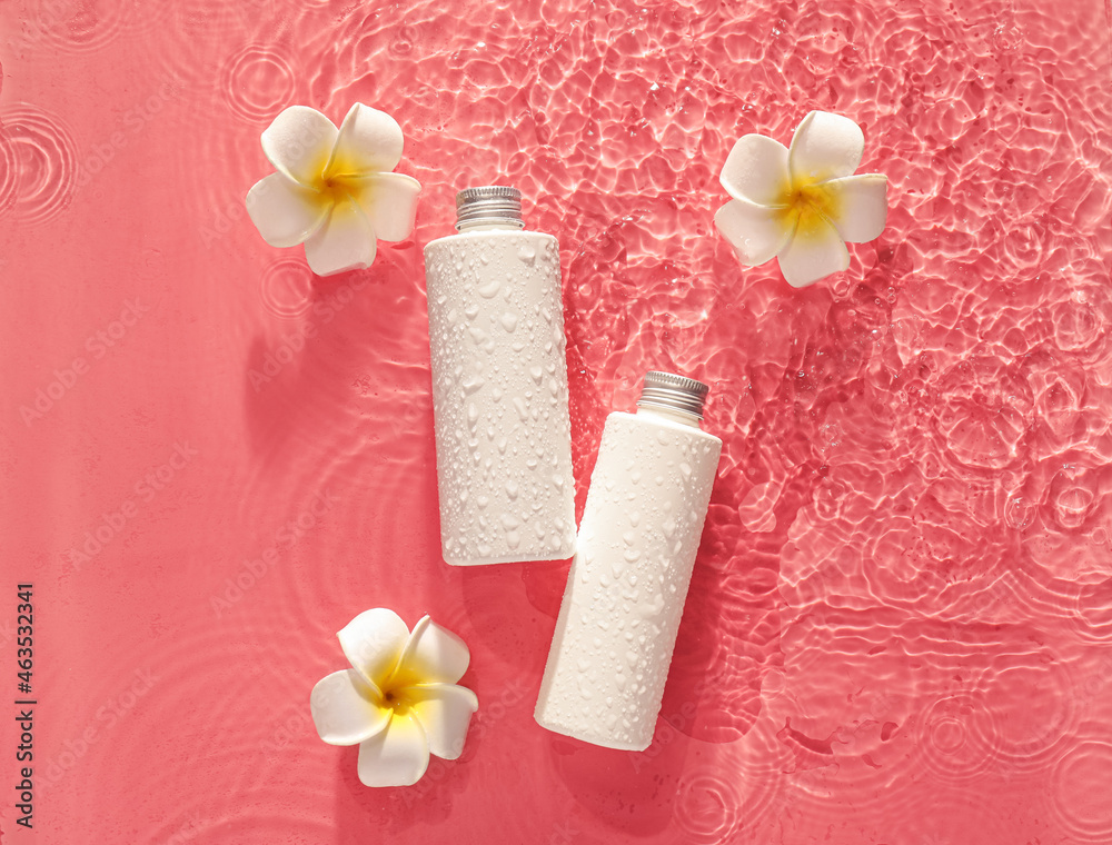 Bottles of cosmetic products and plumeria flowers in water on color background