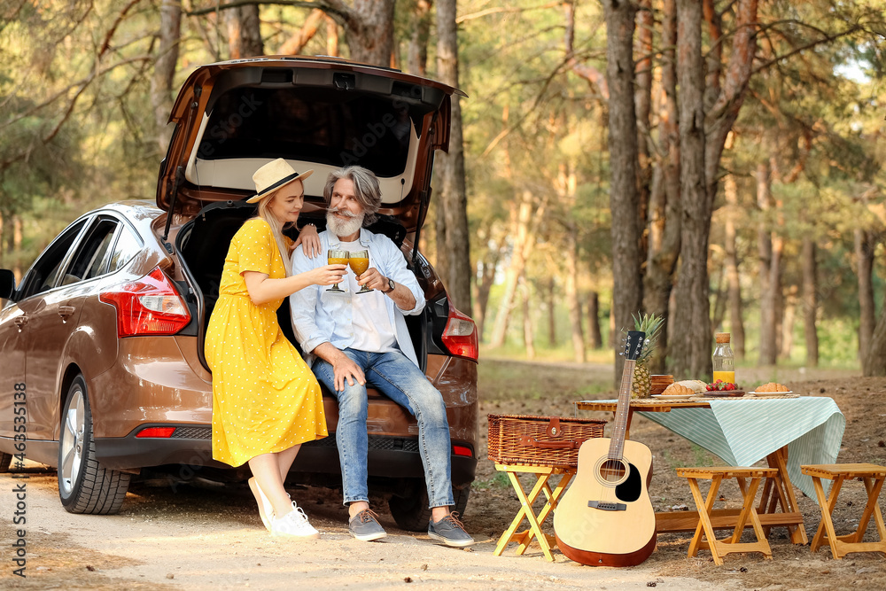 Happy mature couple drinking juice near car in forest