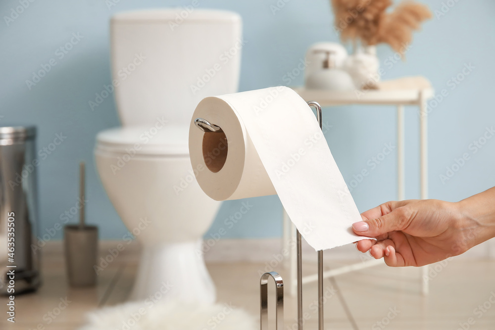 Woman tearing off toilet paper in light restroom, closeup