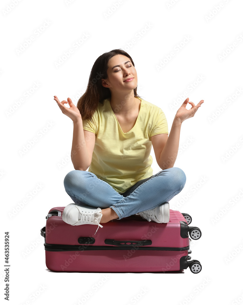 Young woman with suitcase meditating on white background