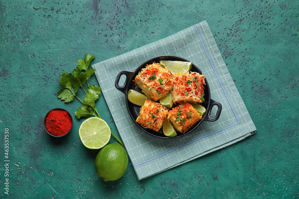 Frying pan with tasty Elote Mexican Street Corn, lime and pepper on green background