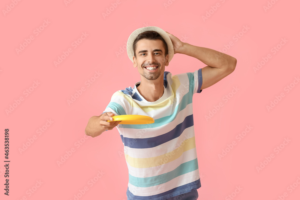 Handsome young man throwing frisbee on pink background