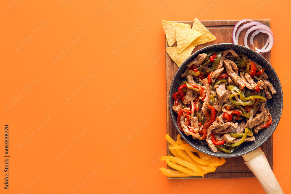 Frying pan with delicious beef Fajita and vegetables on color background