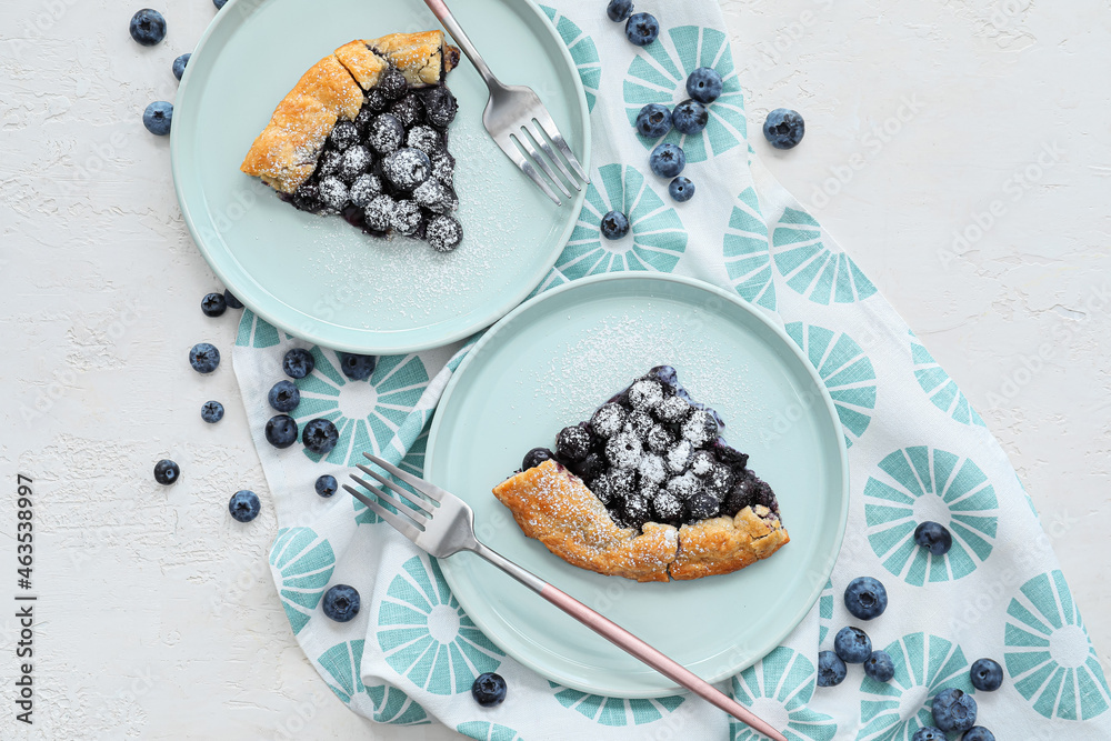 Plates with pieces of tasty blueberry galette on light background