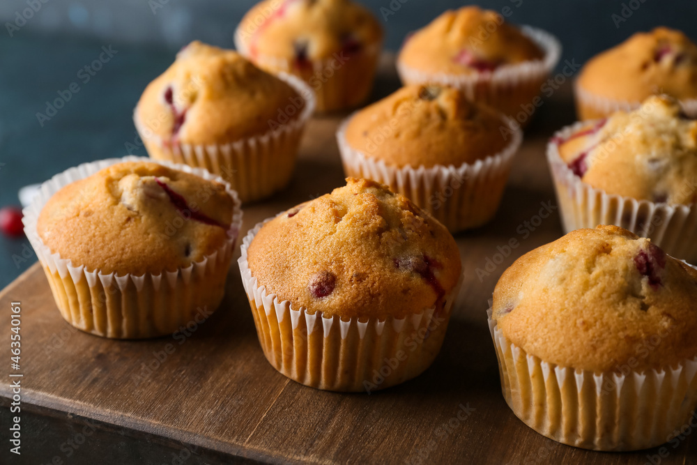 Wooden board with delicious cranberry muffins on table, closeup