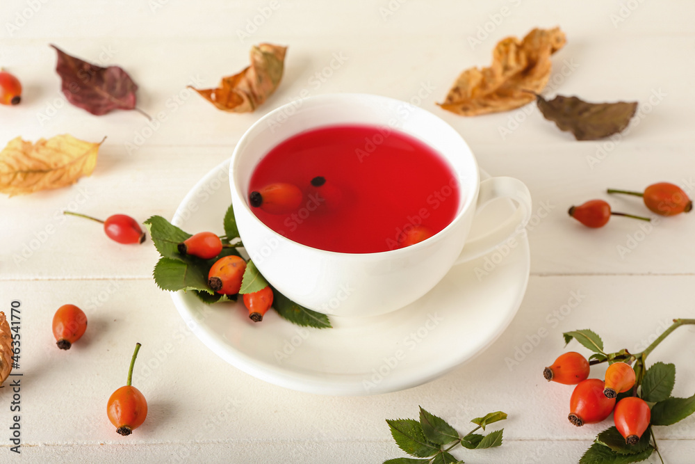 Cup of tasty rose hip tea and berries on white wooden background