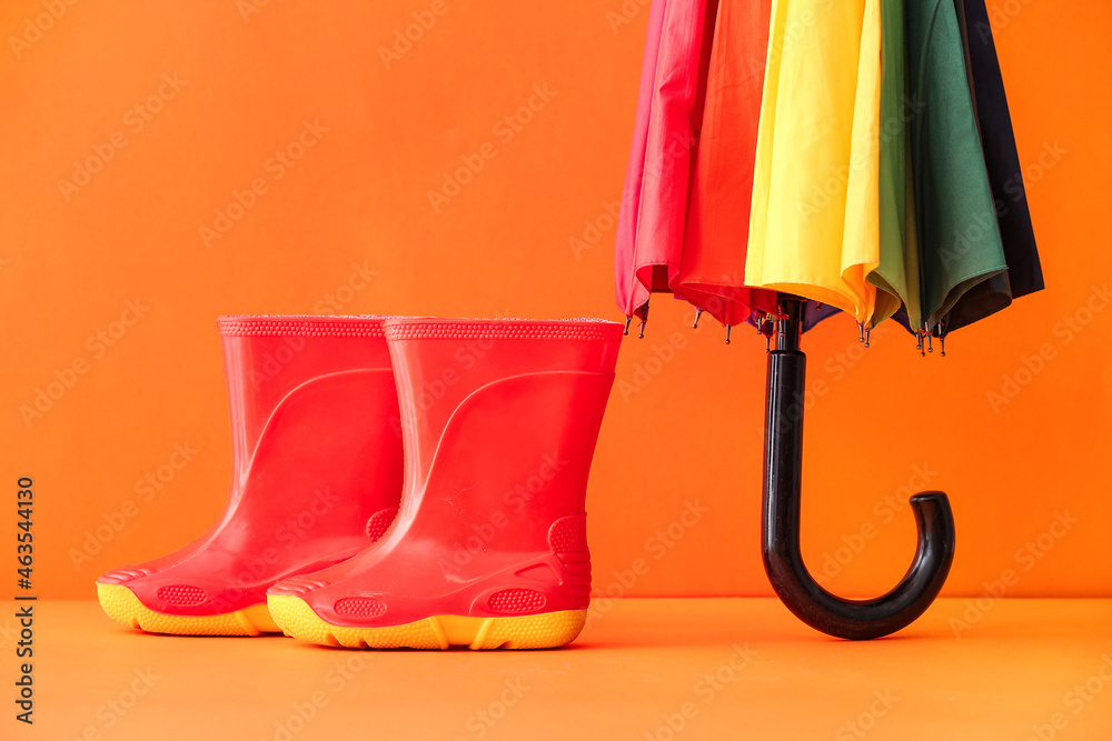 Rubber boots and umbrella on color background, closeup