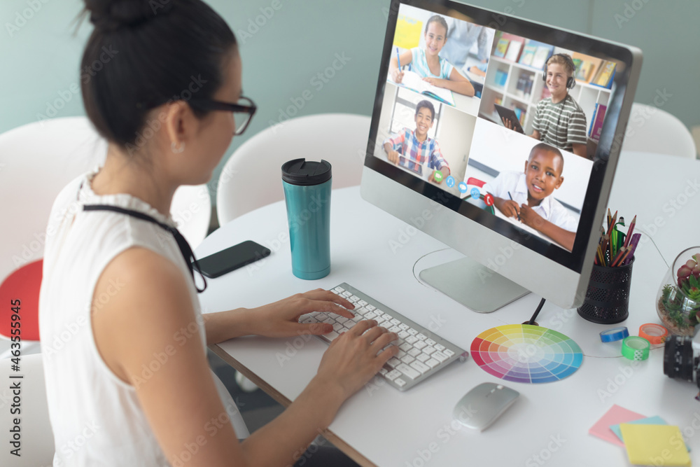 Asian girl using computer for video call, with smiling diverse high school pupils on screen