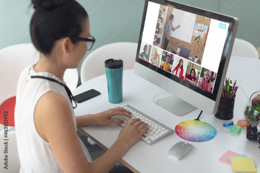 Asian girl using computer for video call, with smiling diverse elementary school pupils on screen