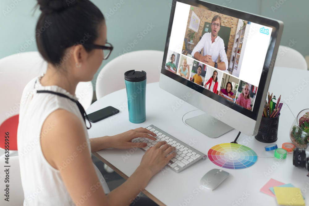 Asian girl using computer for video call, with smiling diverse elementary school pupils on screen