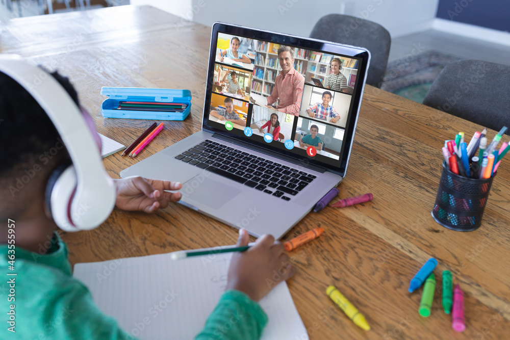 African american boy using laptop for video call, with diverse elementary school pupils on screen