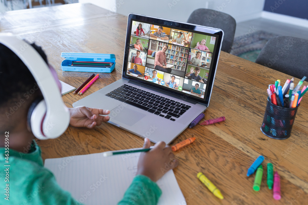 African american boy using laptop for video call, with diverse elementary school pupils on screen