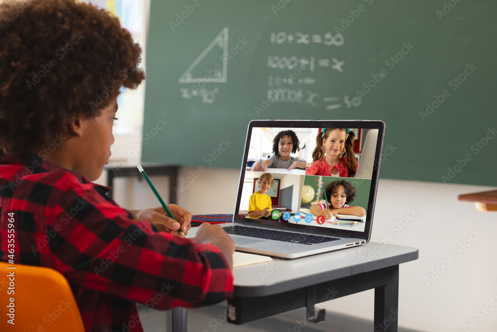 African american boy using laptop for video call, with diverse elementary school pupils on screen