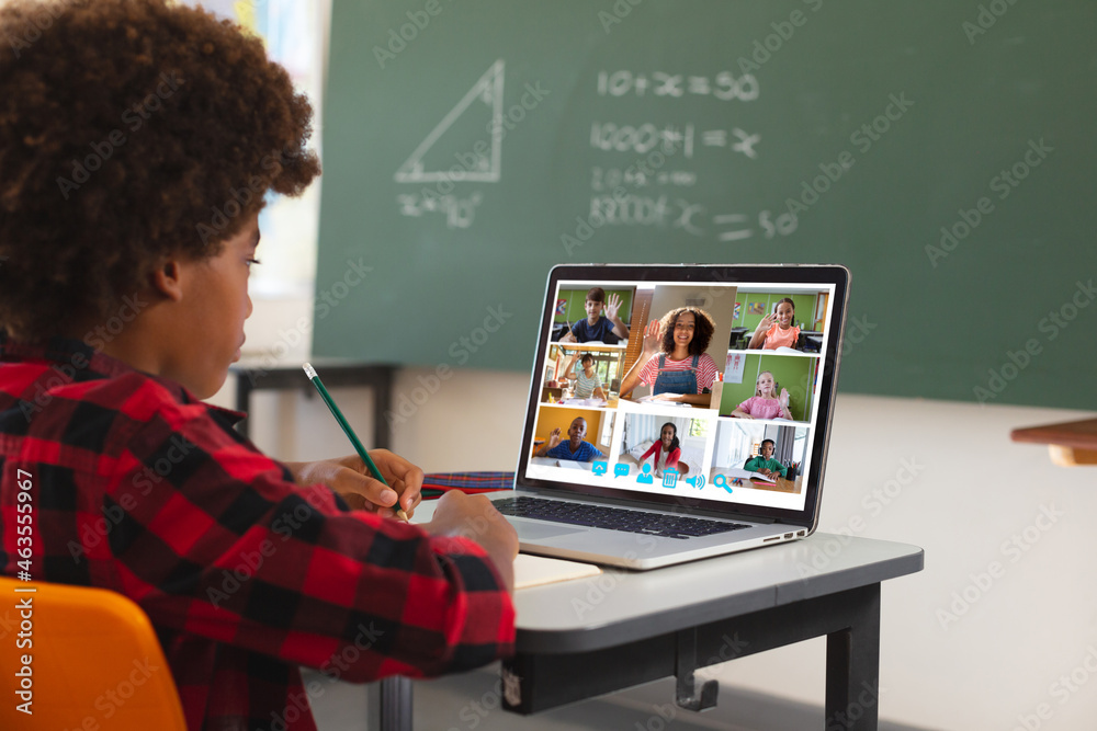 African american boy using laptop for video call, with diverse elementary school pupils on screen