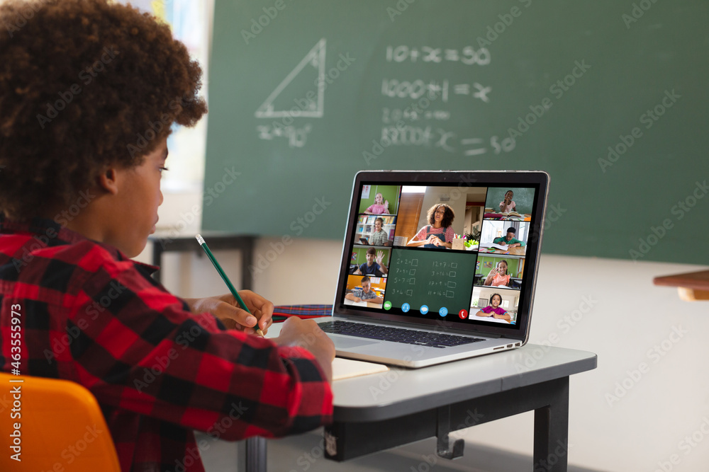 African american boy using laptop for video call, with diverse elementary school pupils on screen