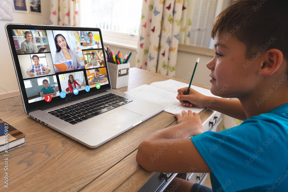 Caucasian boy using laptop for video call, with smiling diverse high school pupils on screen