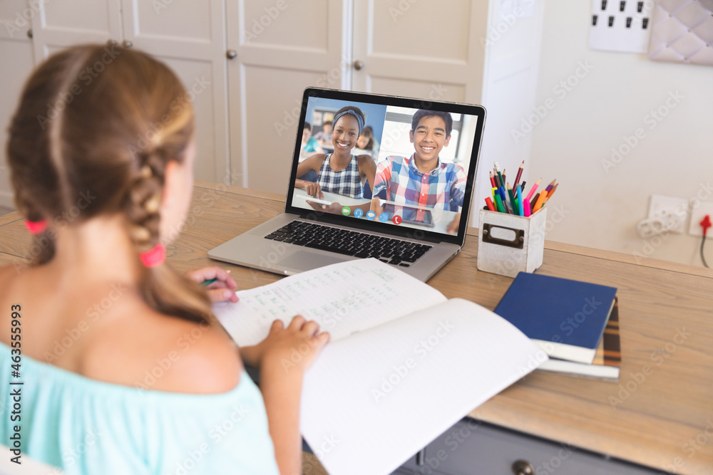 Caucasian girl using laptop for video call, with smiling diverse high school pupils on screen