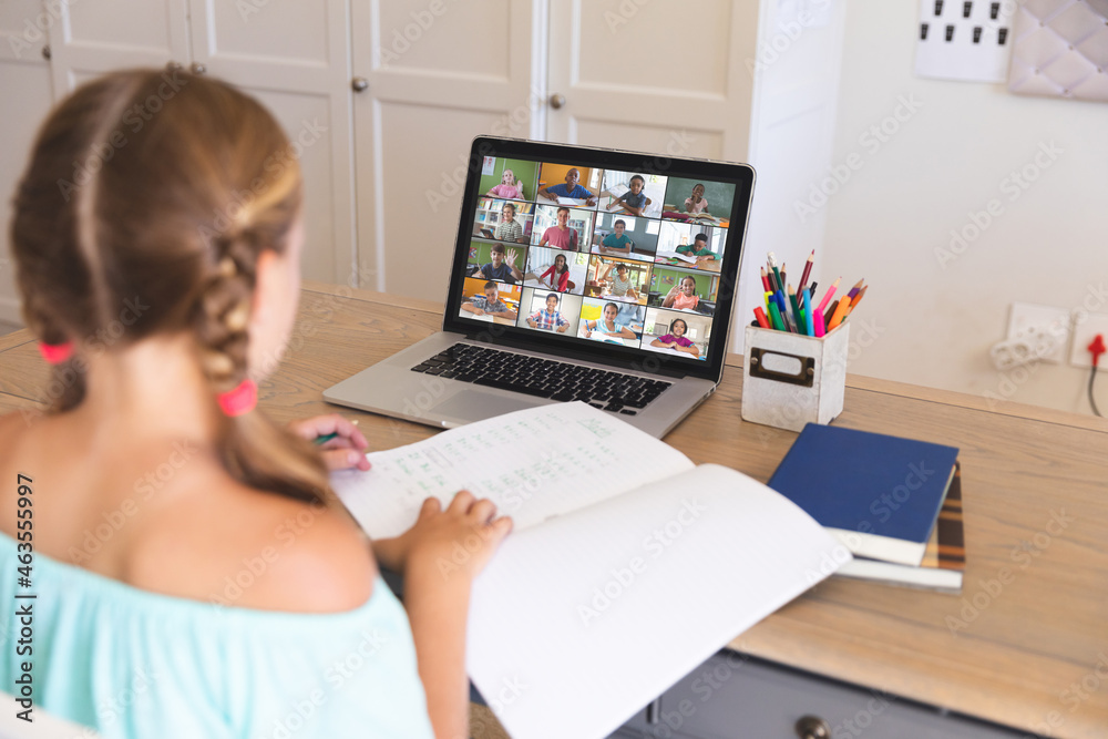 Caucasian girl using laptop for video call, with smiling diverse elementary school pupils on screen