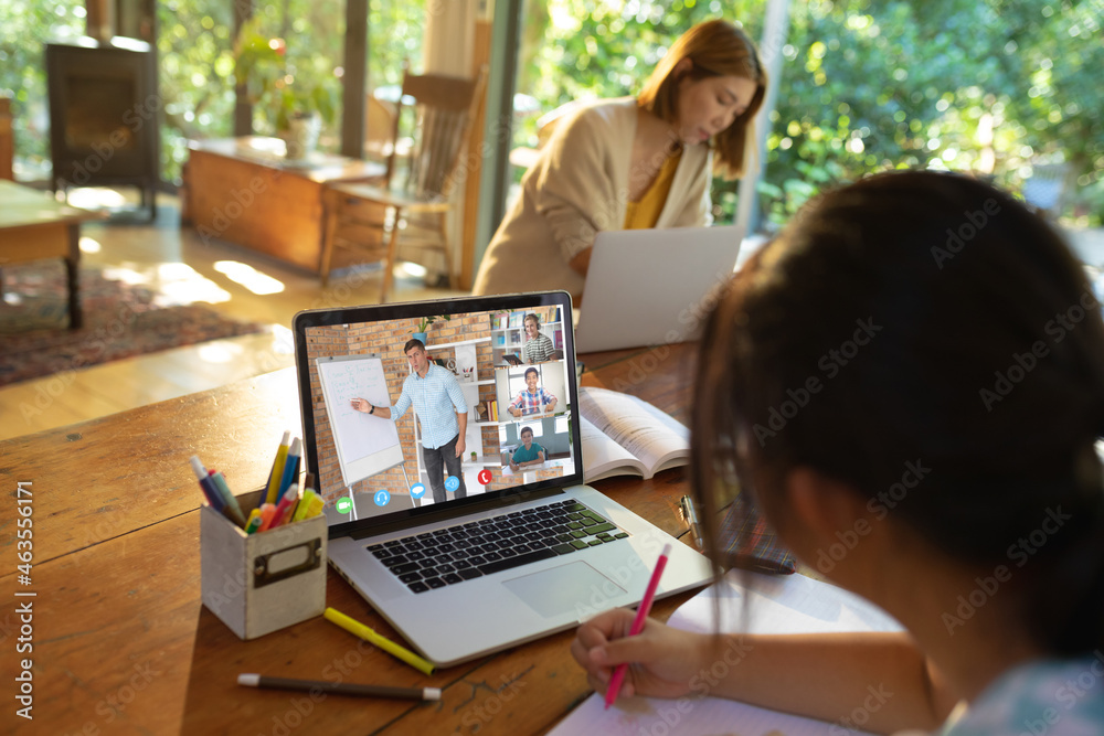 Asian girl using laptop for video call, with smiling diverse elementary school pupils on screen