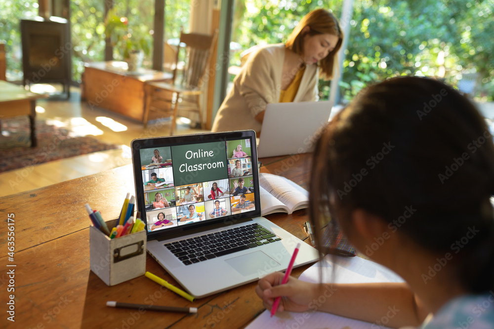 Asian girl using laptop for video call, with smiling diverse elementary school pupils on screen