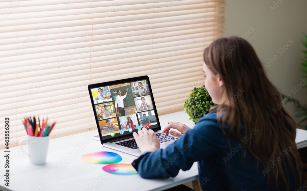 Caucasian girl using laptop for video call, with smiling diverse elementary school pupils on screen